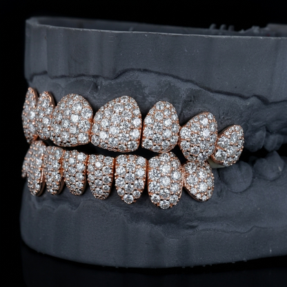 Rose gold moissanite grillz on a dark gray dental mold, low side angle showing top and bottom iced out teeth