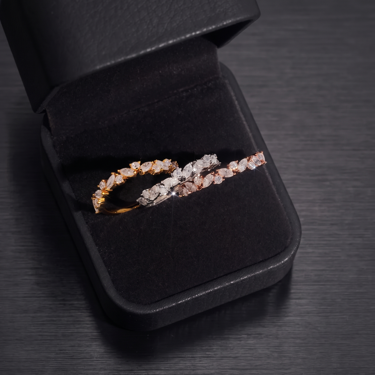 Gold and rose gold marquise moissanite eternity bands in a black ring box on a brushed black metal table