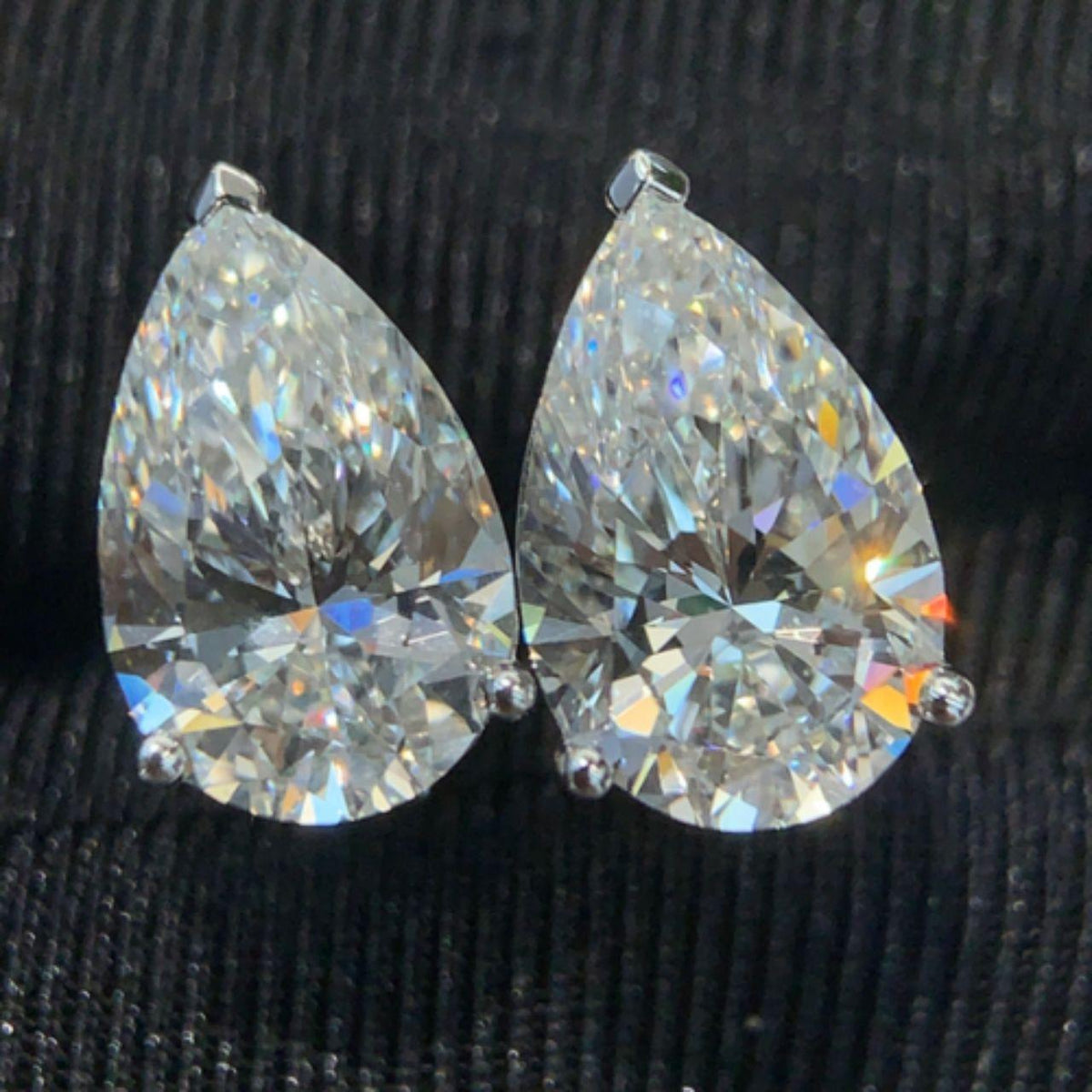 Close macro of both pear cut moissanite studs showing the colored fire and faceting across the stone